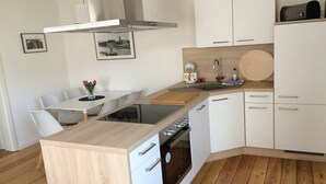 Et moderne køkken med hvide skabe, en træbordplade, indbygget ovn og et spiseområde med et hvidt bord og stole.