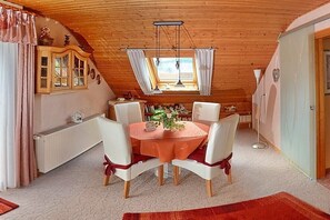 En spiseplads med et rundt bord, hvide stole og et træloft.