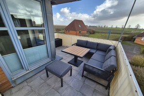 An outdoor patio with a sectional sofa, a small table, and a bench. - Holiday apartment with 1 bedroom (Friedrichskoog)
