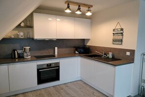 A modern kitchen with white cabinets, a built-in oven, a microwave, and a coffee maker. - Holiday apartment with 1 bedroom (Friedrichskoog)