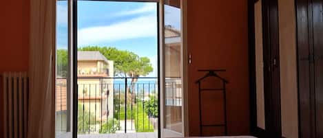 A bedroom with a bed, a view of a balcony, and a door.