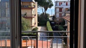 A view from a balcony with a metal railing, overlooking a residential area with buildings, a tree, and a clear sky.