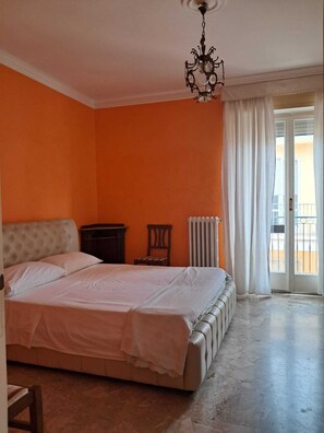 A bedroom with a large bed, a radiator, a chair, and a window with curtains.