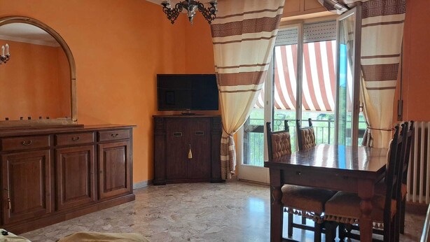 A room with a wooden cabinet, a television, a dining table with chairs, a chandelier, and a window with curtains.