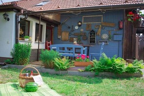 A house with a blue exterior, a garden with various plants, a picnic setup, and a blue bench. - Holiday home with 2 bedrooms (Byhleguhre)