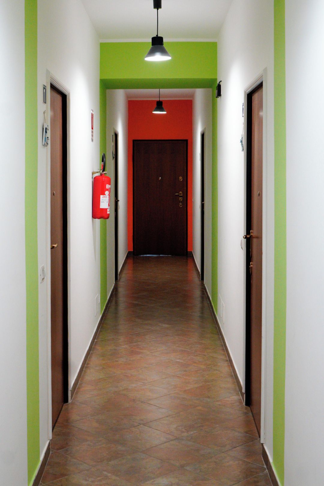 Un pasillo con paredes verdes, una puerta roja al final y un extintor en la pared izquierda.