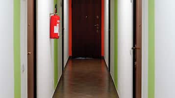 Un pasillo con paredes verdes, una puerta roja al final y un extintor en la pared izquierda.