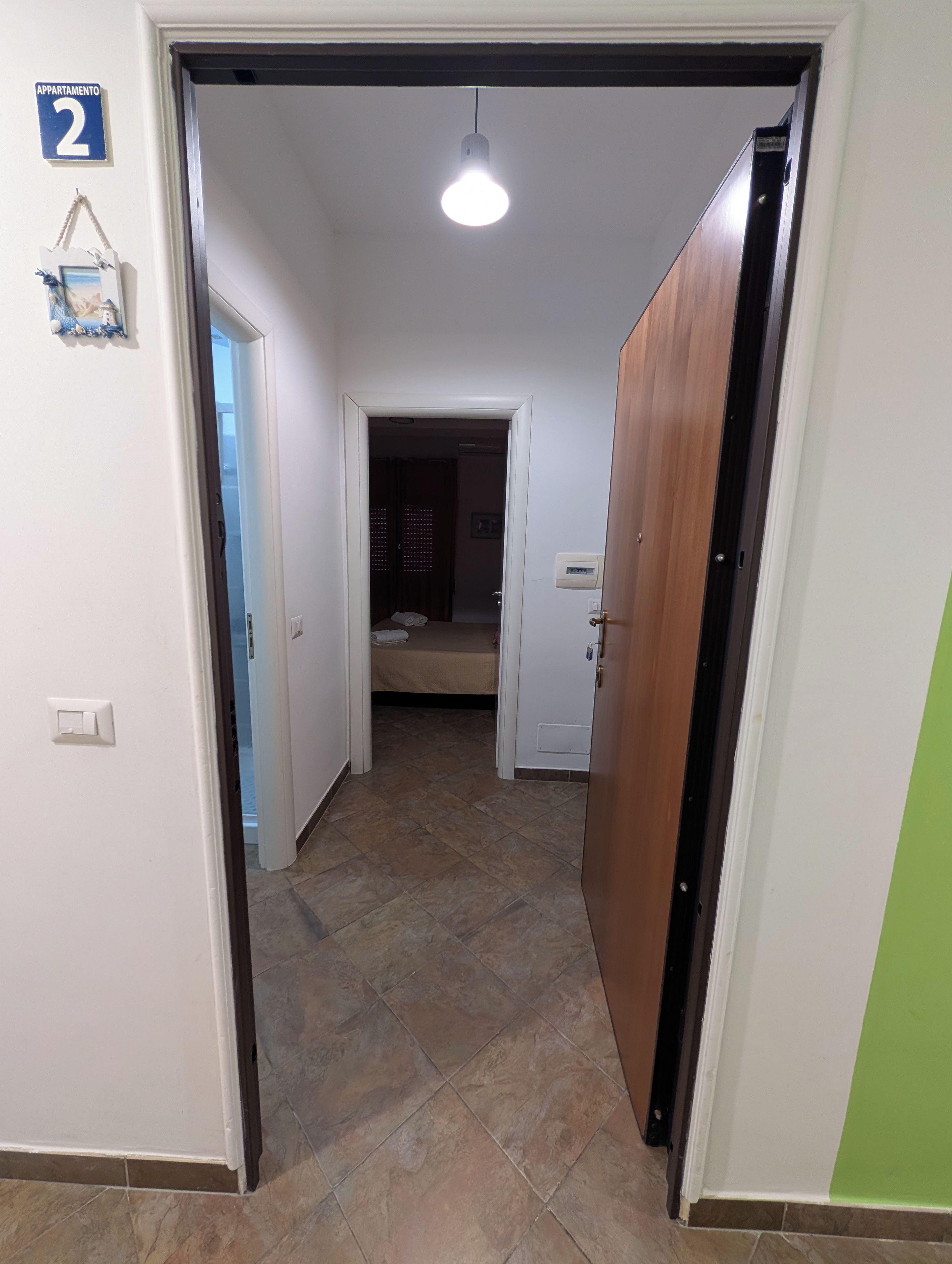 A hallway with a tiled floor, a door on the right, and a bed in the background.