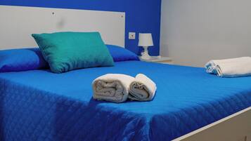 Ein Bett mit blauer Bettwäsche, einem türkisfarbenen Kopfkissen und zwei gerollten weißen Handtüchern.