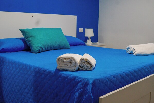 A bed with blue bedding, a teal pillow, and two rolled white towels.