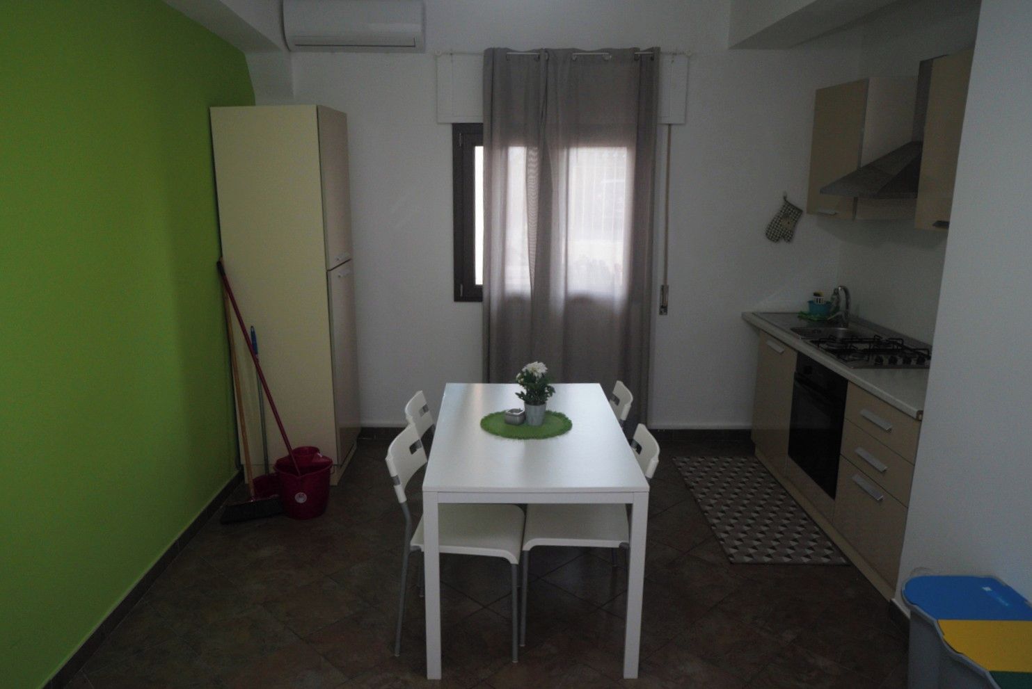 A compact kitchen with a dining table, chairs, a refrigerator, and a window with curtains.