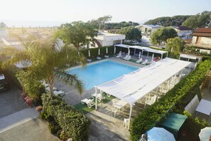 Una piscina con tumbonas y una zona de estar cubierta, rodeada de vegetación y edificios residenciales.