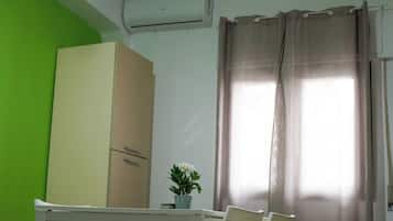 Een kamer met een groene wand, een beige kledingkast, een tafel met stoelen, een kamerplant en een raam met gordijnen.