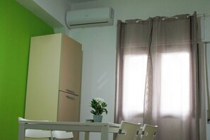 Una habitación con una pared verde, un armario color beige, una mesa con sillas, una planta en maceta y una ventana con cortinas.