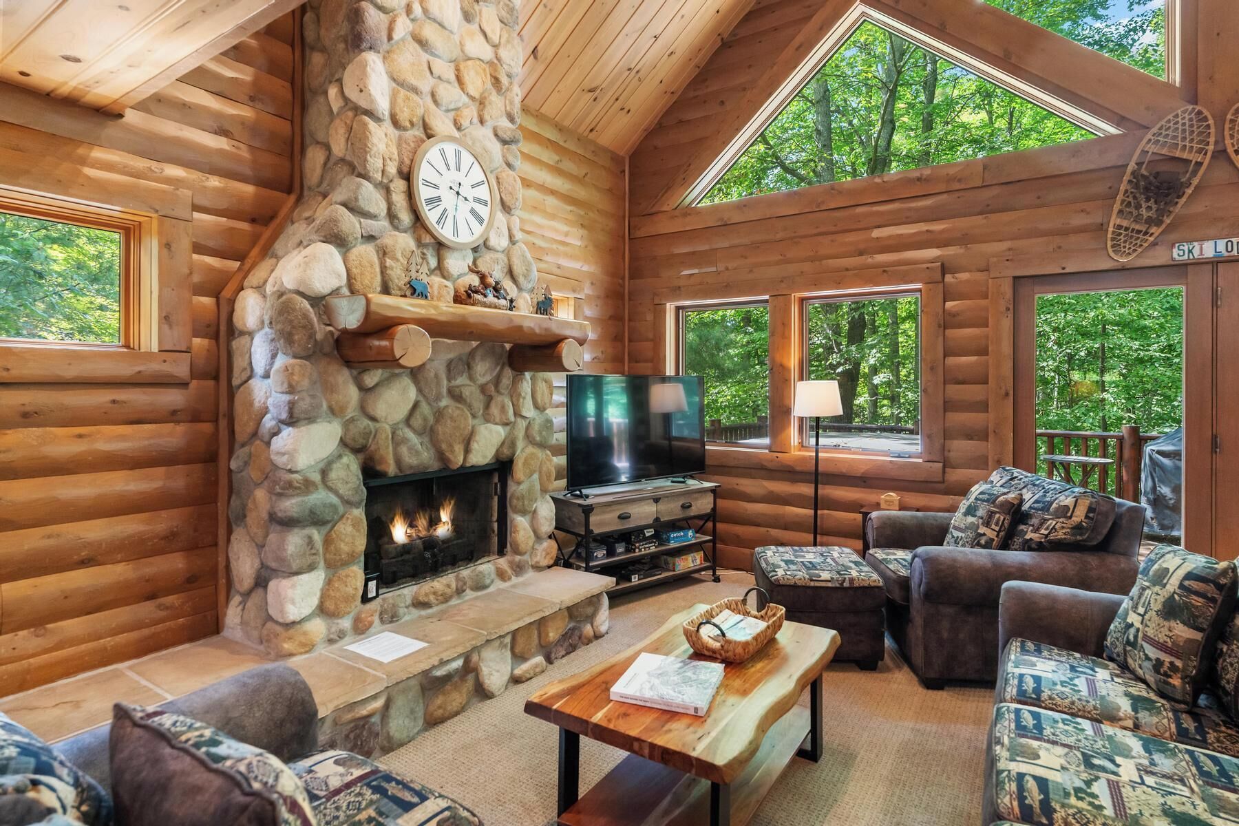 L’intérieur d’une cabane en rondins, avec une cheminée en pierre, un téléviseur et un coin salon confortable.