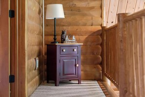 A wooden cabin interior with a small dresser, a lamp, and a decorative item on top. - Cozy Log Cabin Retreat with Hot Tub (Boyne City)