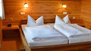 Quarto estilo cabana de madeira com uma cama de casal, duas luminárias fixadas na parede e uma mesinha de cabeceira.