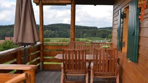 Um deck de madeira com mesa e cadeiras, com vista para uma paisagem arborizada.