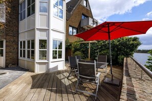 Eine Holzterrasse mit einem roten Sonnenschirm, einem Tisch und Stühlen.