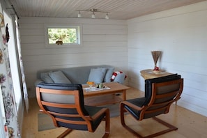 Ett rum med en soffa, två stolar, ett litet bord, ett fönster och en takfläkt.