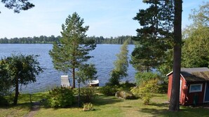 A lakeside property with a red cabin, a dock, and a grassy area with trees.