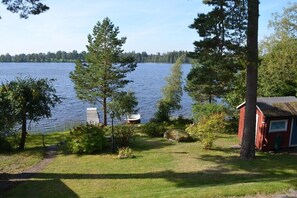 A lakeside property with a red cabin, a dock, and a grassy area with trees.