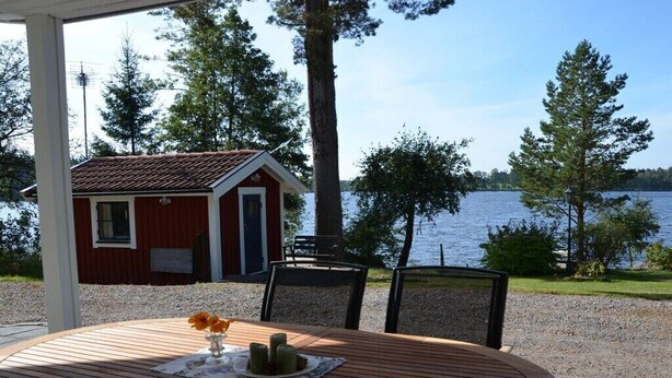 A wooden table with a vase and candles, overlooking a lake with a red building in the background.