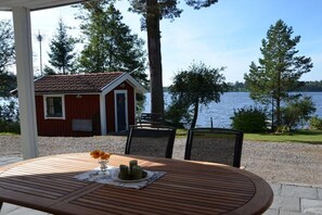Ein Holztisch mit einer Vase und Kerzen, mit Blick auf einen See, im Hintergrund ein rotes Gebäude.