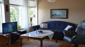 A living room with a blue sofa, a black leather chair, a wooden coffee table, and a television on a desk.