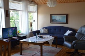 A living room with a blue sofa, a black leather chair, a wooden coffee table, and a television on a desk.
