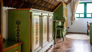 A room with a herringbone patterned wooden floor, a green cabinet with decorative panels, and a window with green shutters.