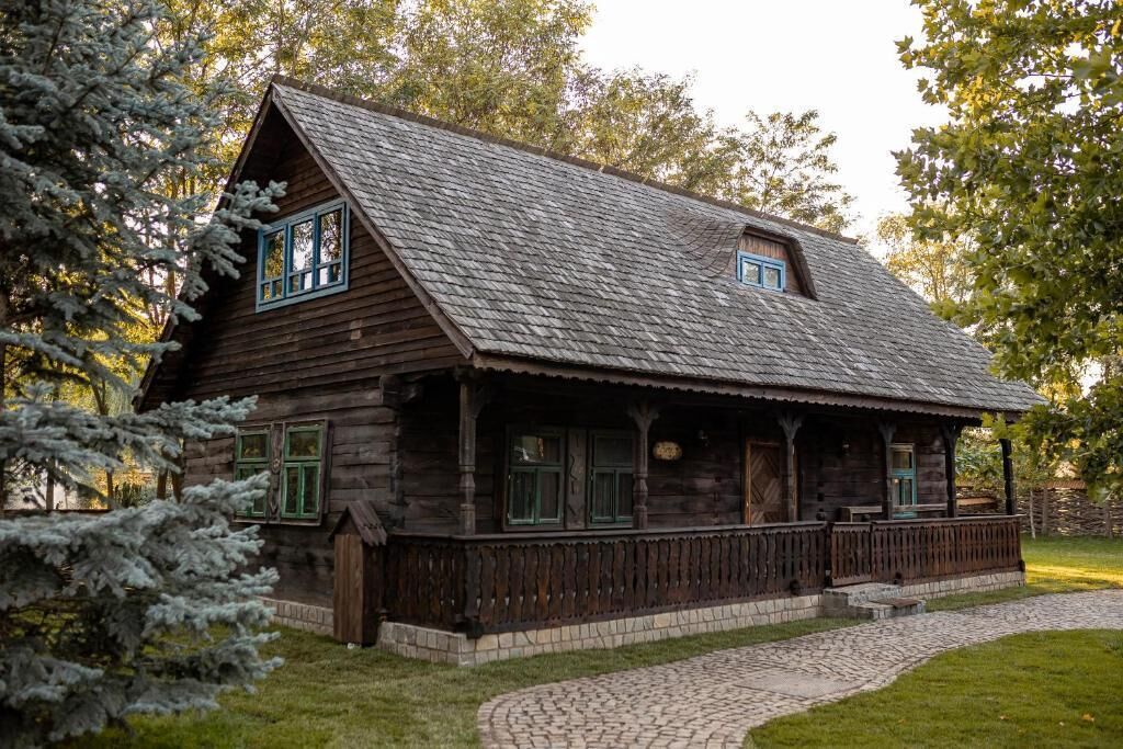 A rustic wooden cabin with a sloped roof, a porch with railings, and a stone pathway leading to the entrance.