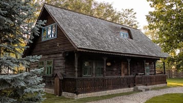 A rustic wooden cabin with a sloped roof, a porch with railings, and a stone pathway leading to the entrance.