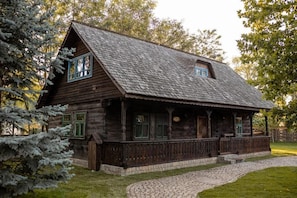A rustic wooden cabin with a sloped roof, a porch with railings, and a stone pathway leading to the entrance.
