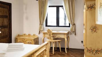 A room with a bed, a wooden desk, a chair, a wardrobe, and a window with curtains.