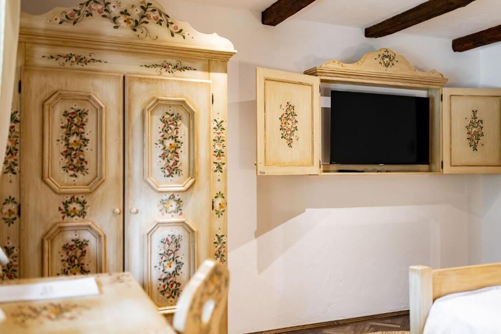 A room with a bed, a television mounted on a wall, and a wooden wardrobe with floral designs.