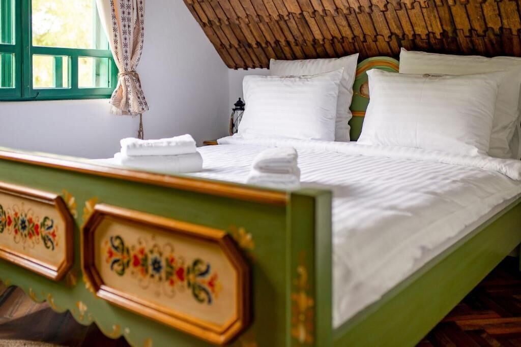 A bed with white linens, a wooden headboard with decorative patterns, and a green wall.