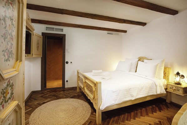 Un dormitorio con una cama de madera, ropa de cama blanca, un tapete redondo y una mesita de noche con una lámpara.