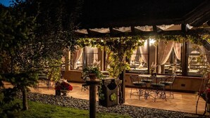 An outdoor patio area with a table and chairs, surrounded by a pergola with climbing plants.