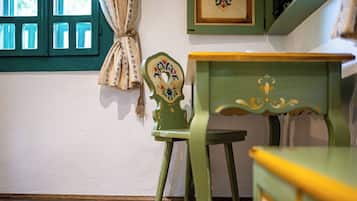 A room with a wooden herringbone floor, a green chair with a decorative backrest, and a small table with a green top and yellow trim.