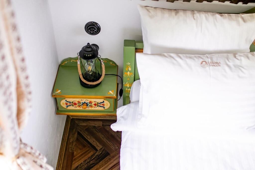 Cama com roupa de cama branca e mesa de cabeceira verde com abajur decorativo.