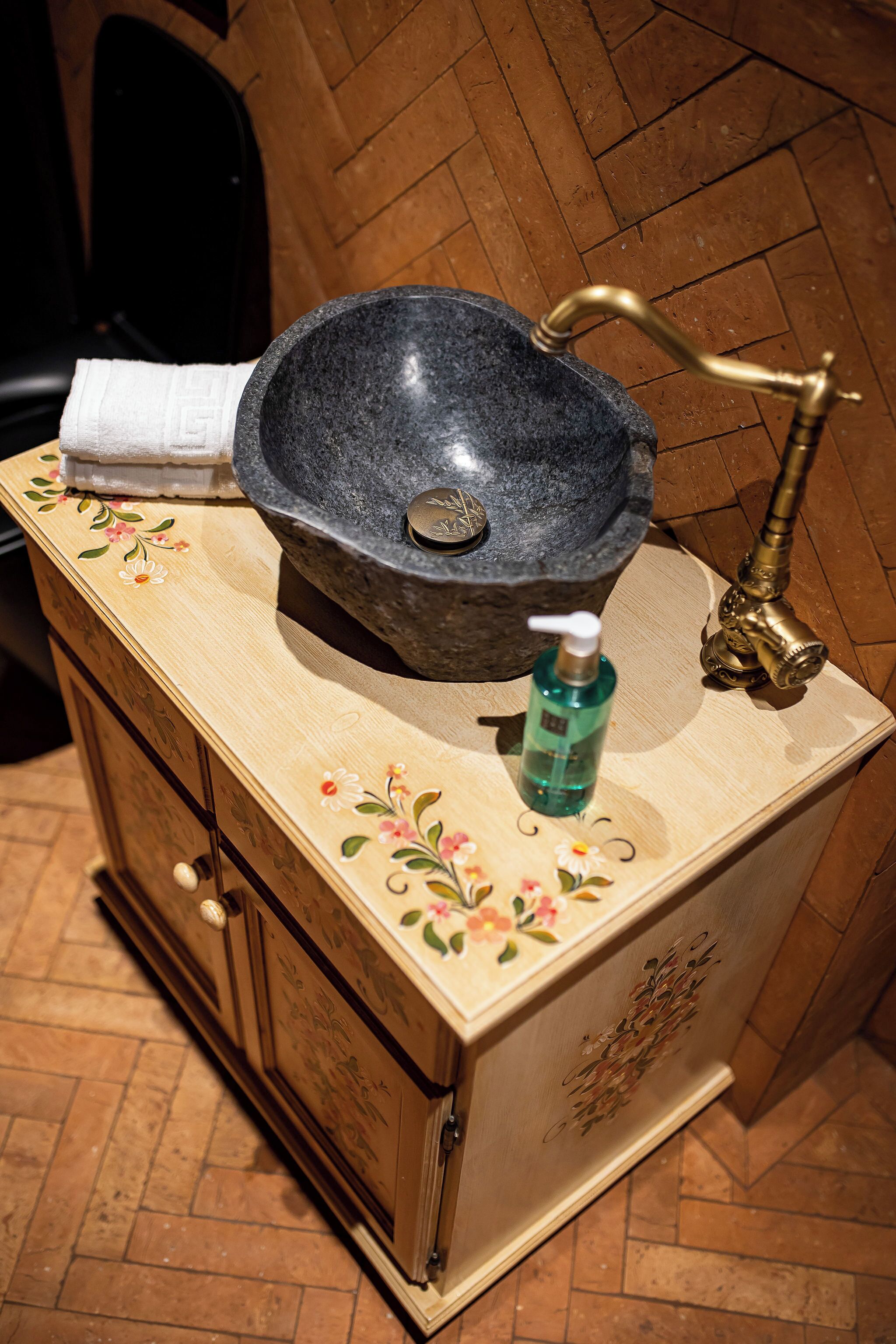 Un lavamanos de baño con lavabo de piedra, un grifo y una botella de jabón para manos.