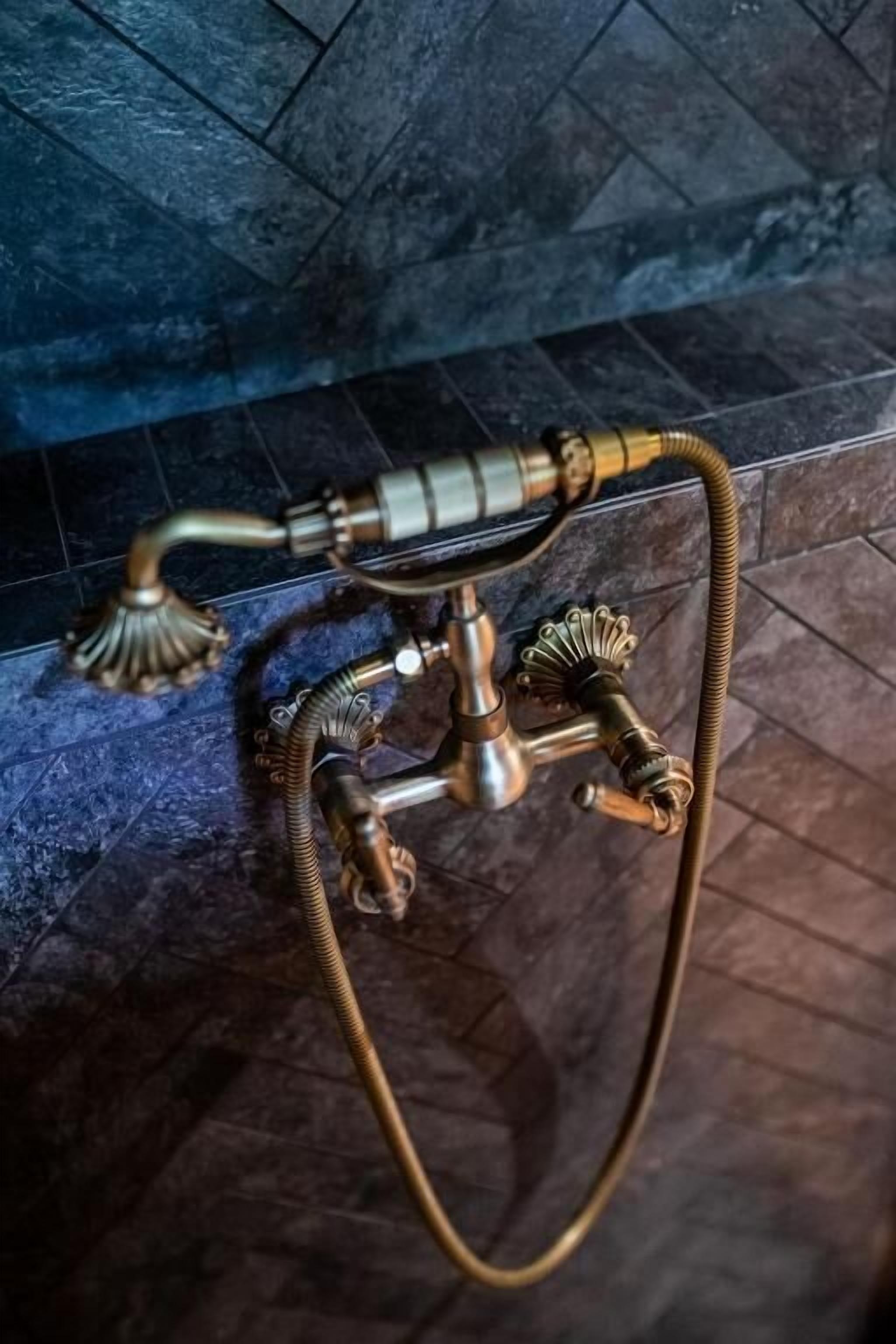A brass water heater with a flexible hose, placed on a tiled floor.