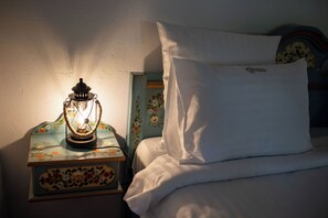 Una cama con ropa de cama blanca, una almohada blanca y un farol decorativo en una mesita de noche.