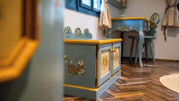 A room with a wooden floor, a blue cabinet with floral designs, a chair, and a table with a blue tablecloth.