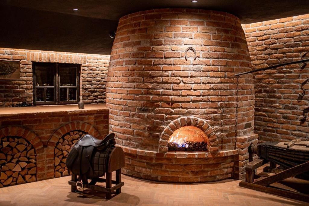 A brick oven with a fire burning inside, surrounded by stone walls and a wooden bench.