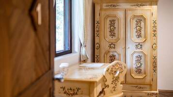 A room with a wooden wardrobe, a table with a floral tablecloth, and a window with curtains.