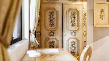 Habitació amb una porta de fusta decorada amb motius florals, una taula amb mantell floral i una finestra amb cortines.