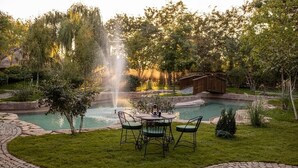 A garden with a fountain, a pool, and a wooden deck.