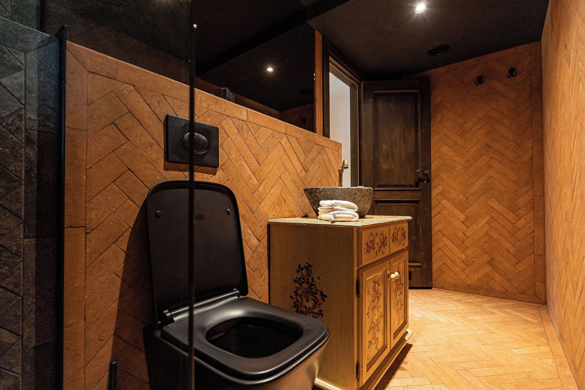 Un baño moderno con un inodoro negro, paredes de madera y un suelo con estampado tipo espiga.
